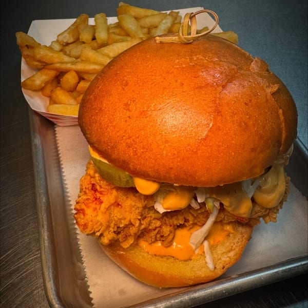 Flamin Feathers fried chicken sandwich with pickles, sauce, and fries on a metal tray.