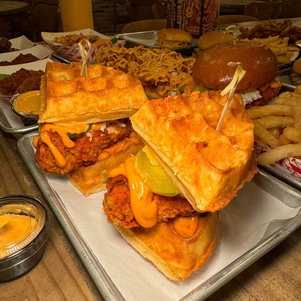 Two Flamin Feathers fried chicken and waffle sandwiches with sauce and pickles on a metal tray.