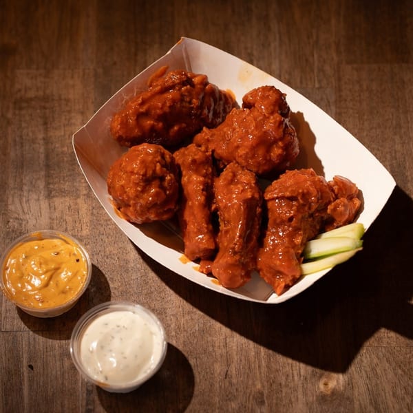Flamin Feathers' spicy fried chicken wings in a paper tray with celery sticks and two dipping sauces.