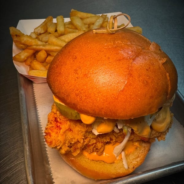 Flamin Feathers fried chicken sandwich with pickles, sauce, and shredded lettuce, served with fries.