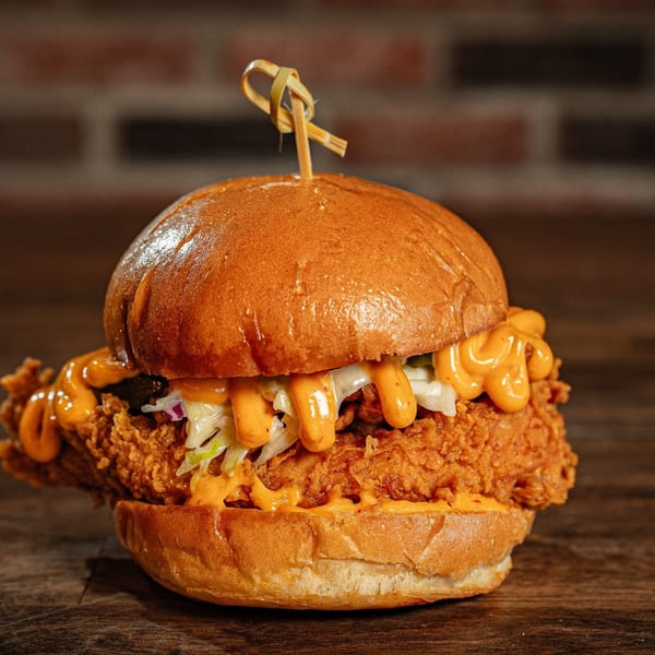 Flamin Feathers fried chicken sandwich with orange sauce and coleslaw on a brioche bun.