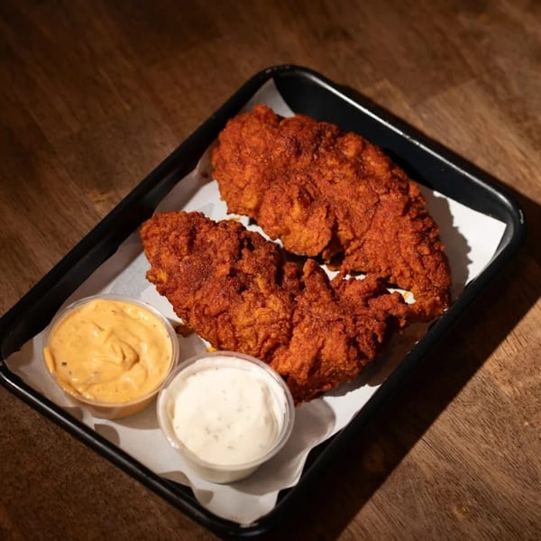 Two crispy Flamin Feathers fried chicken tenders with two dipping sauces on a black tray.