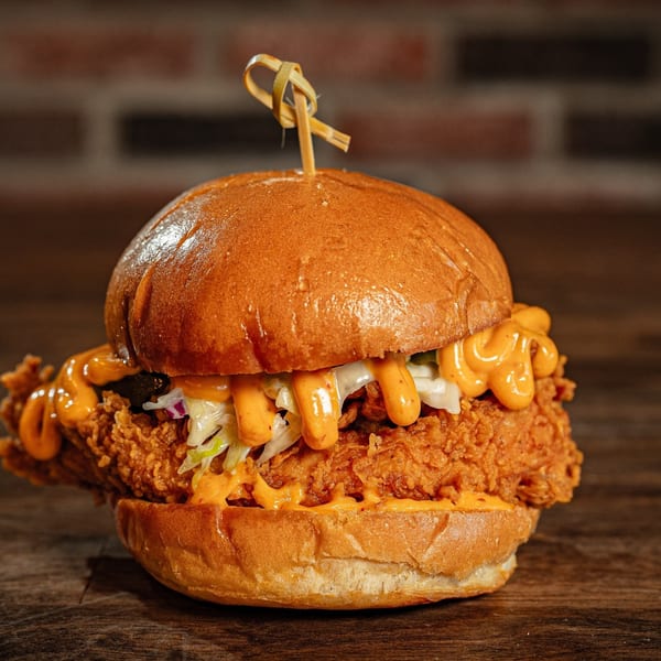 Flamin Feathers' fried chicken sandwich with coleslaw and orange sauce on a wooden table.