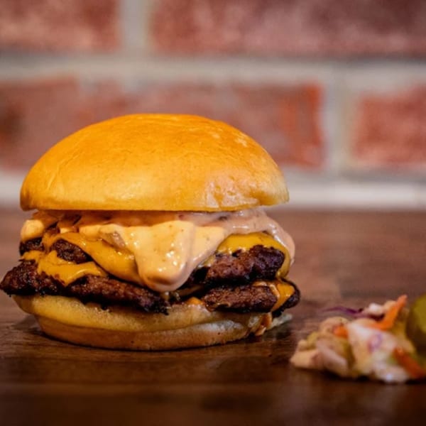 Double smash burger with melted cheese and sauce, served with coleslaw on a wooden table.