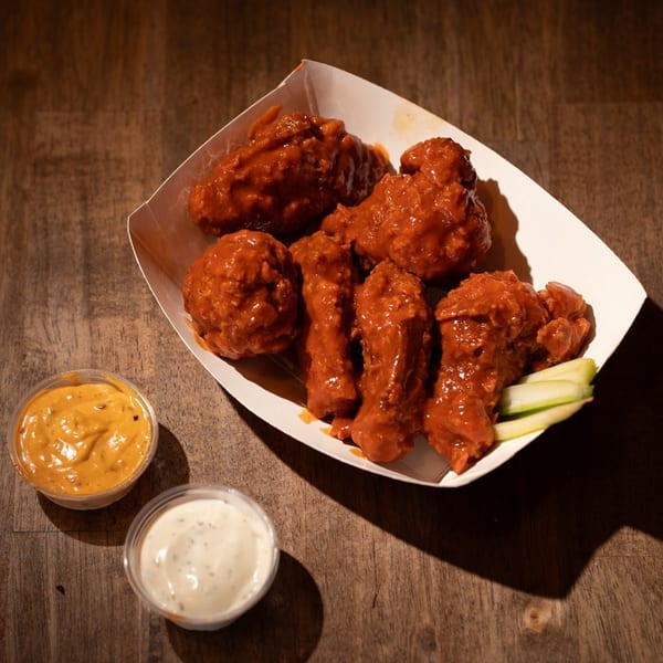 Flamin Feathers' spicy fried chicken wings in a paper tray with two dipping sauces and celery.