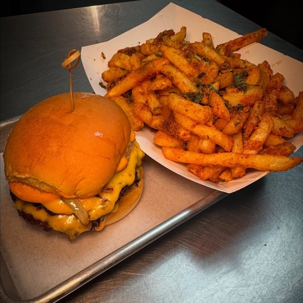 A double cheeseburger with melted cheese and onions next to a container of seasoned fries.
