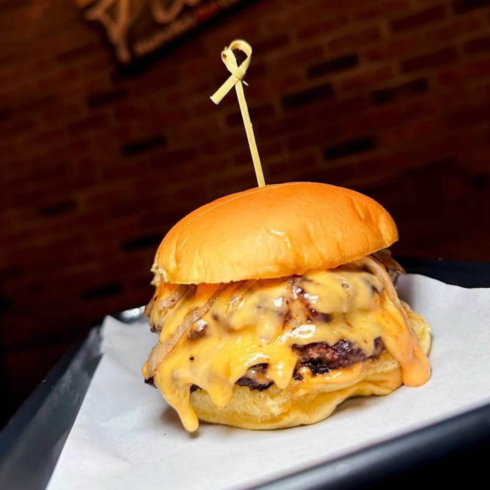 A Flamin Feathers burger with melted cheese and caramelized onions on a brioche bun.