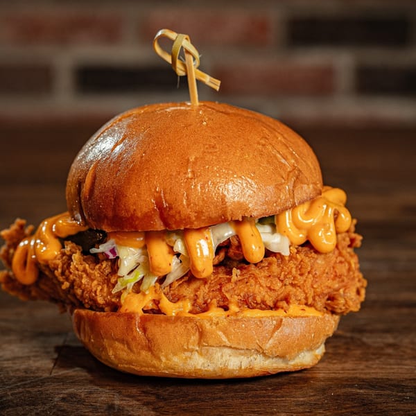 Flamin Feathers fried chicken sandwich with coleslaw and orange sauce on a brioche bun.