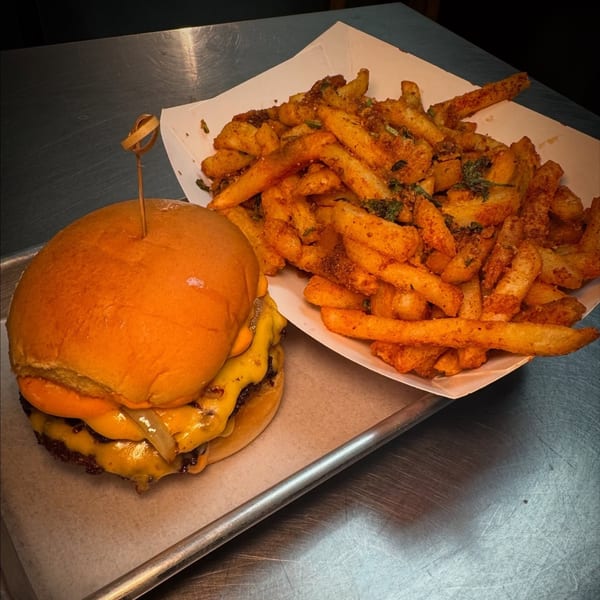 Cheeseburger with melted cheese and grilled onions, next to a container of seasoned fries.