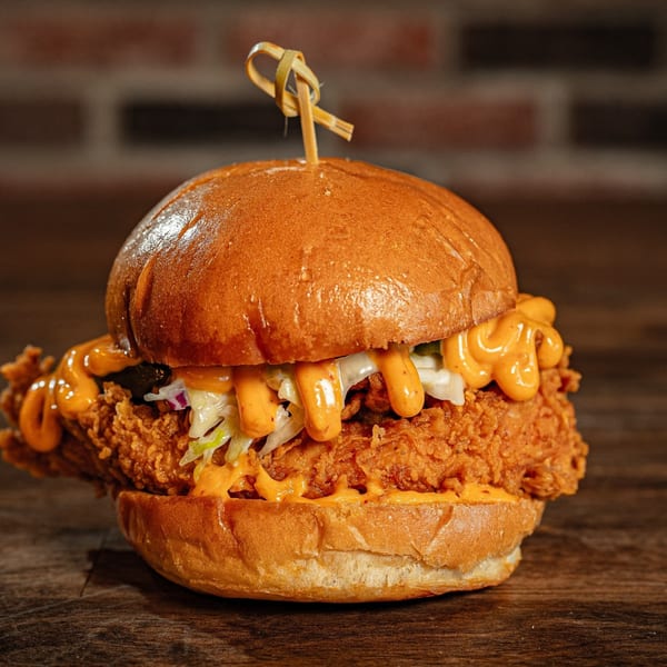 Flamin Feathers fried chicken sandwich with coleslaw and orange sauce on a wooden table.