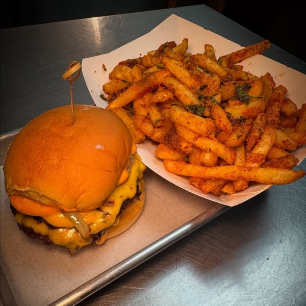 A double cheeseburger with melted cheese and onions, next to a container of seasoned fries.
