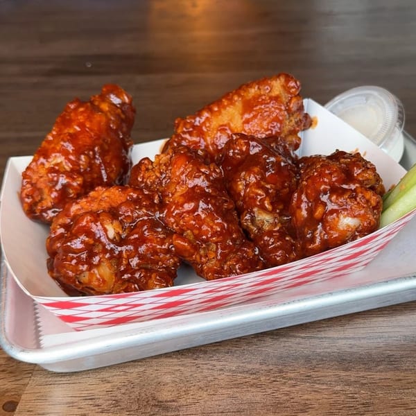 Six Flamin Feathers fried chicken wings, coated in a glossy red sauce, served in a paper tray.